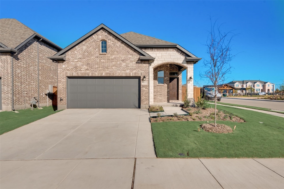 French country inspired facade with brick siding, a front yard, driveway, and roof with shingles