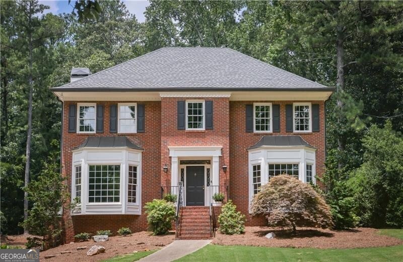 Colonial inspired home featuring brick siding, a chimney, and a shingled roof
