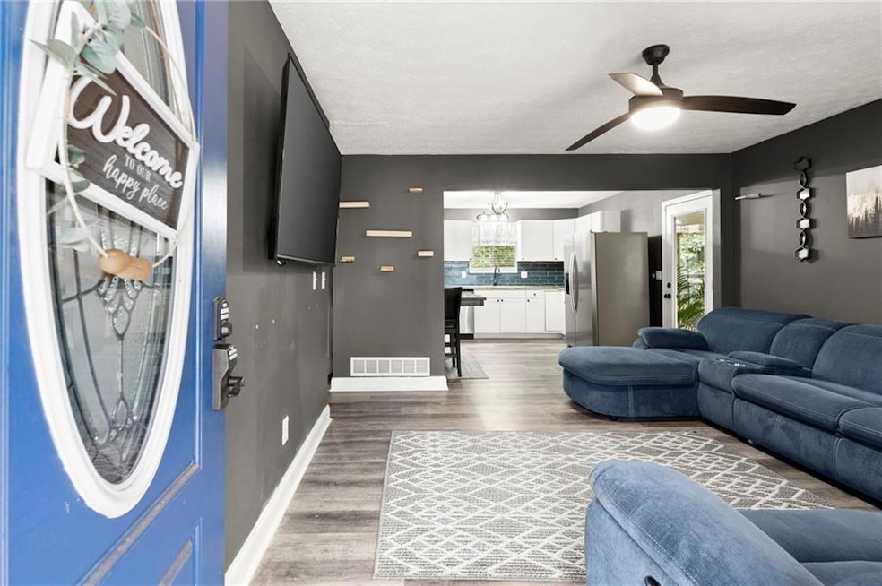 Living area with light wood-style floors, ceiling fan, a chandelier, and a textured ceiling