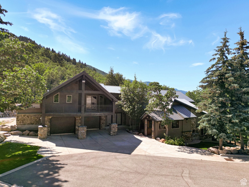 View of front facade featuring stone siding, a garage, concrete driveway, a metal roof, and a standing seam roof