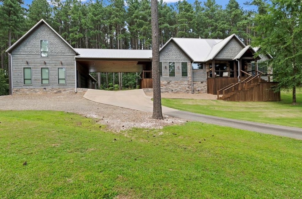 View of front of home with an attached carport, driveway, a front yard, stone siding, and view of scattered trees