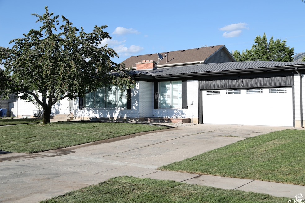 View of front of house featuring driveway, an attached garage, brick siding, a front lawn, and metal roof