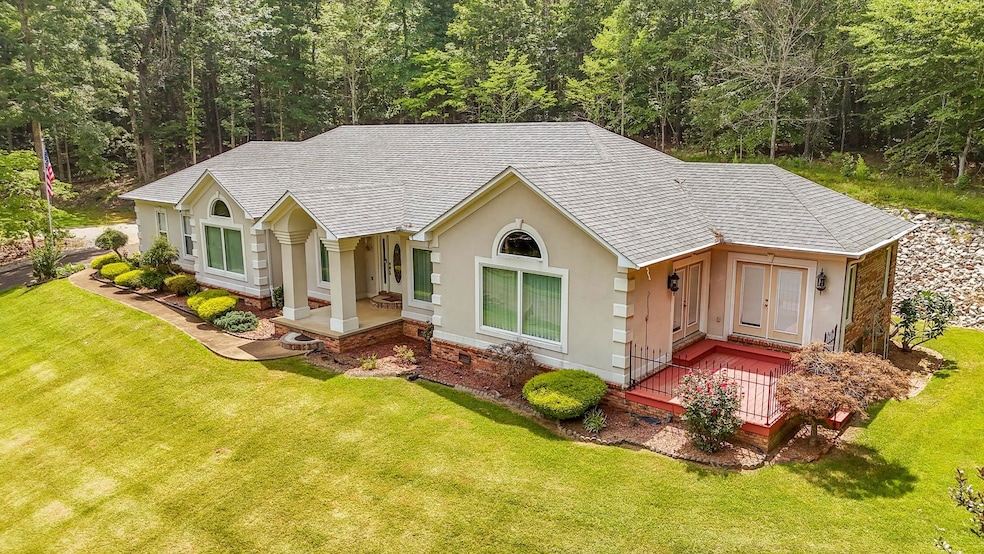 Ranch-style home with roof with shingles, stucco siding, a front lawn, a forest view, and covered porch