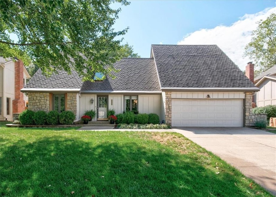 View of front of home with stone siding, a front yard, a shingled roof, concrete driveway, and a garage
