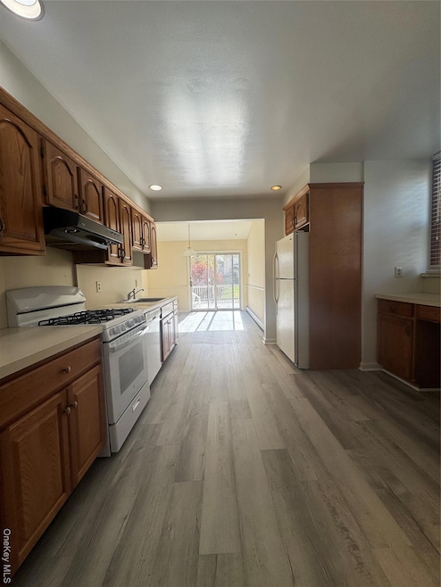 Kitchen with range, light countertops, refrigerator, light wood-type flooring, and exhaust hood