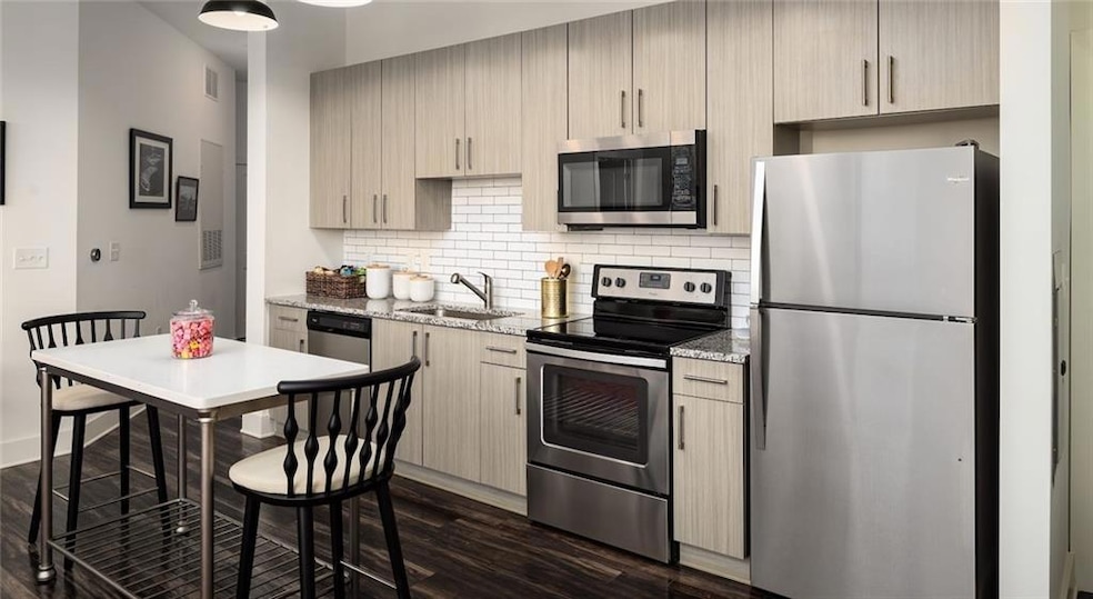Kitchen featuring dark hardwood / wood-style floors, light stone countertops, stainless steel appliances, backsplash, and sink