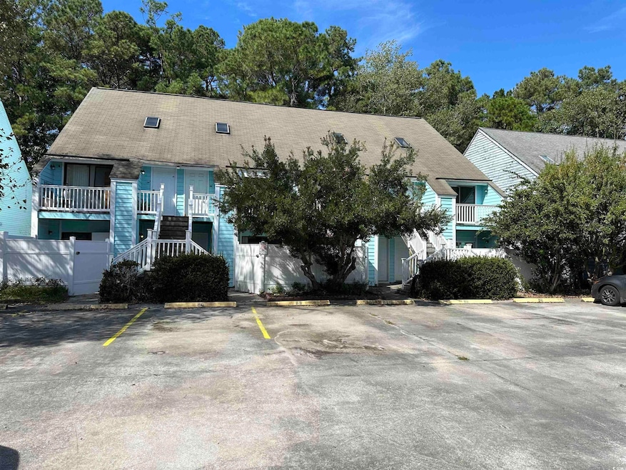 View of front facade with stairway, uncovered parking, a balcony, and view of wooded area