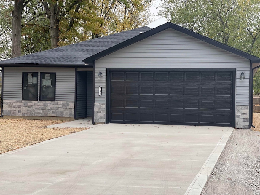 Single story home with stone siding, concrete driveway, roof with shingles, and an attached garage