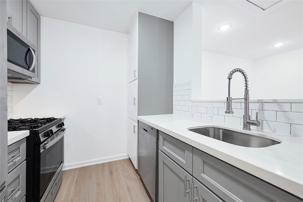 Modern kitchen with sleek gray cabinets, stainless steel appliances, and a tiled backsplash. Features a gas stove, built-in microwave, and a stylish pull-down faucet.