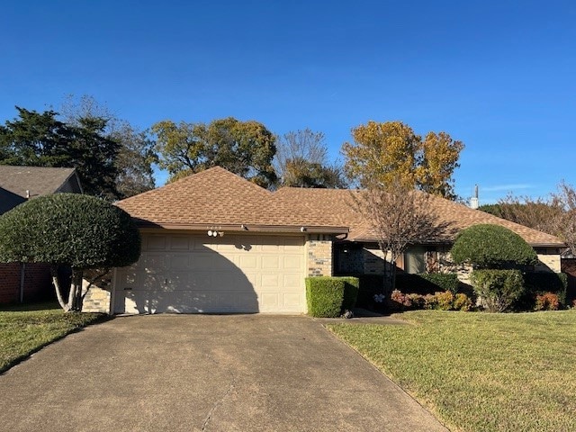 Ranch-style home featuring a front lawn, driveway, an attached garage, and roof with shingles