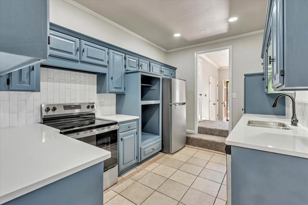 Kitchen with ornamental molding, stainless steel appliances, light tile patterned floors, backsplash, and blue cabinetry