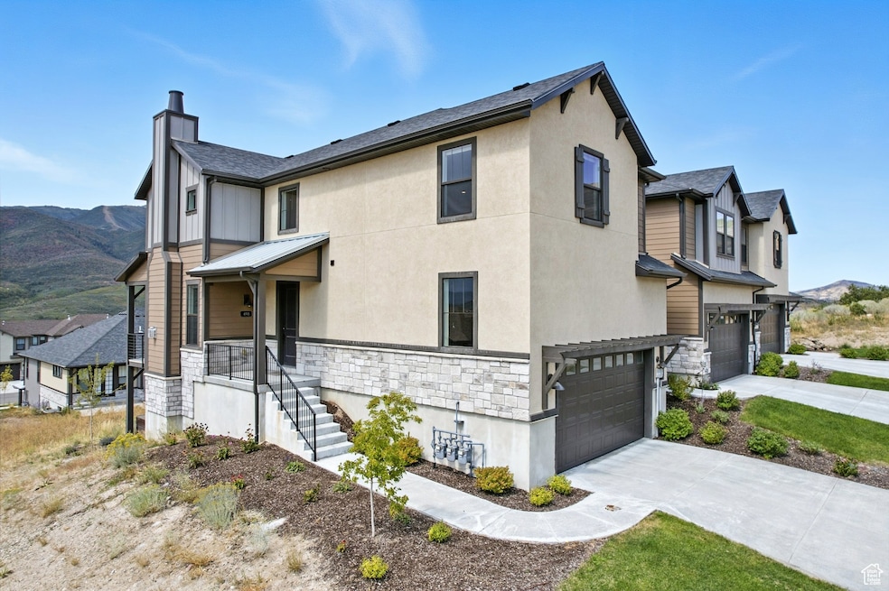 View of property exterior featuring stone siding, a mountain view, an attached garage, driveway, and a chimney