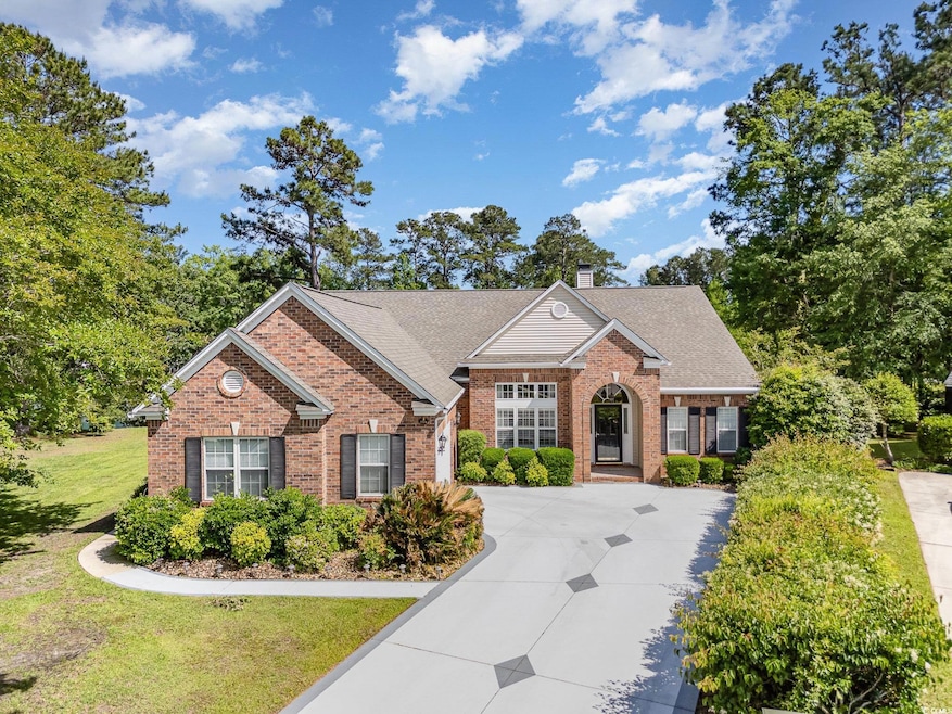 View of front facade featuring driveway, brick siding, a chimney, and a shingled roof