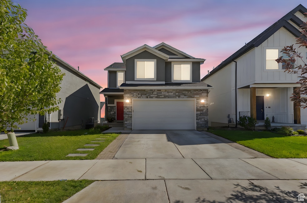 Traditional-style home with driveway, a front yard, an attached garage, and stone siding