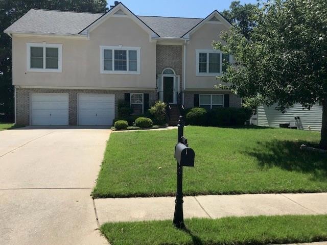 Bi-level home with brick siding, driveway, a front lawn, an attached garage, and stucco siding