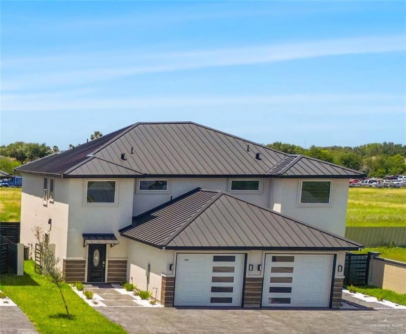 View of front of house with fence, stucco siding, a standing seam roof, driveway, and metal roof