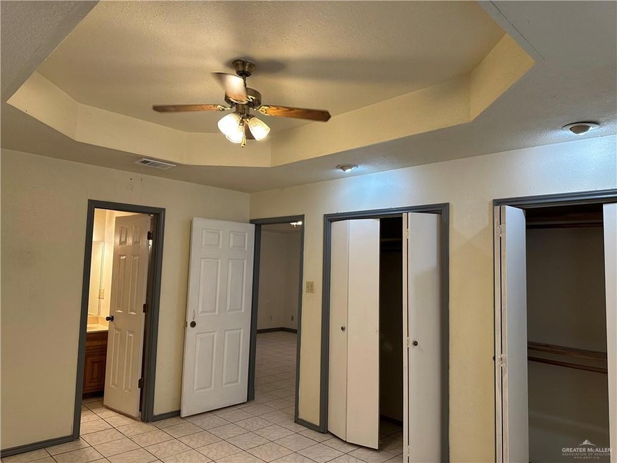 Unfurnished bedroom featuring a raised ceiling, light tile patterned floors, ceiling fan, and connected bathroom