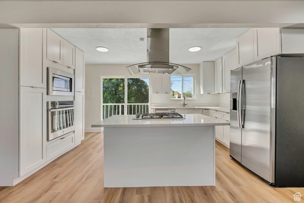 Kitchen with appliances with stainless steel finishes, white cabinetry, island exhaust hood, light wood-type flooring, and recessed lighting