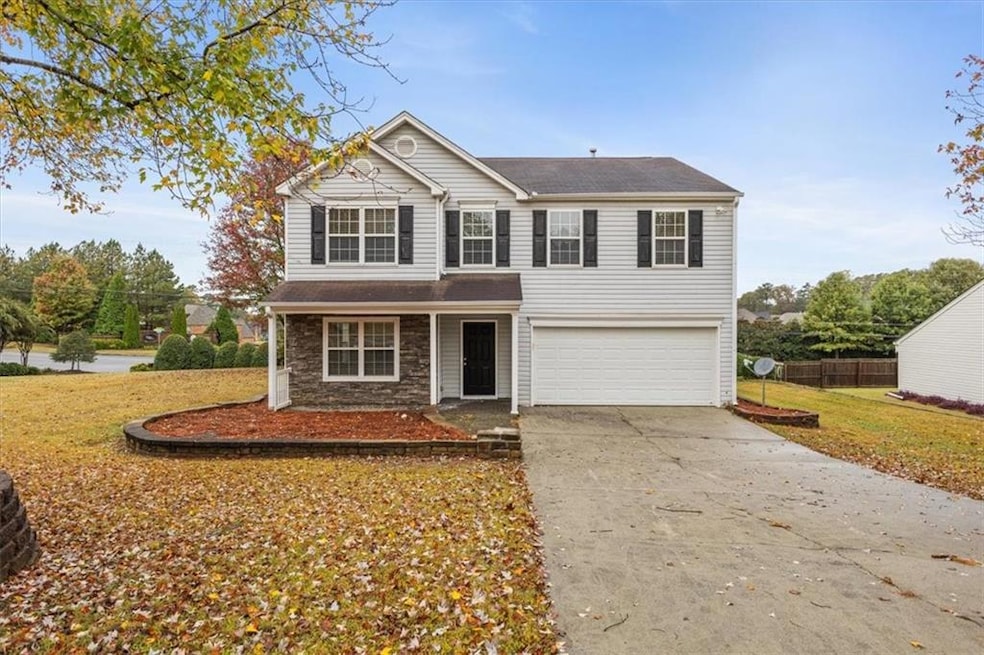 Traditional-style house featuring driveway, stone siding, covered porch, an attached garage, and a front lawn