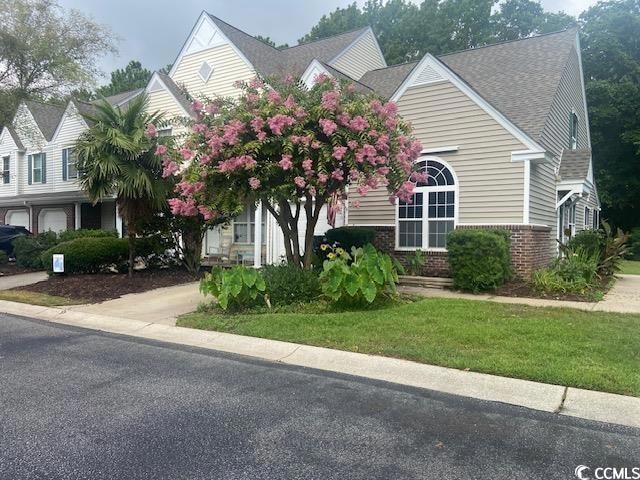 Obstructed view of property featuring brick siding, roof with shingles, and a front lawn