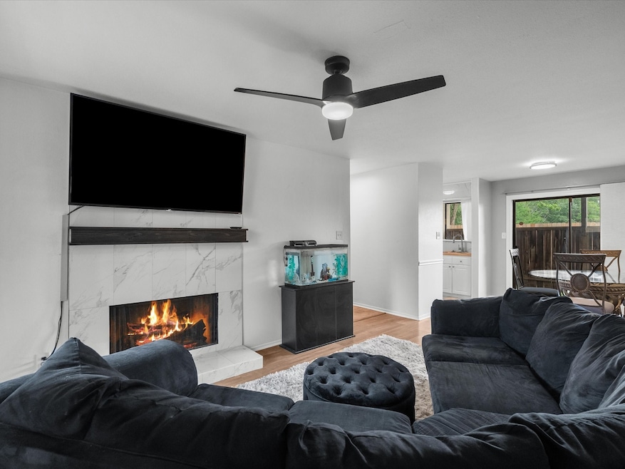 Cozy living room featuring a sleek ceiling fan, inviting fireplace, and seamless flow into the dining area through large sliding doors. Perfect for relaxation and entertaining.