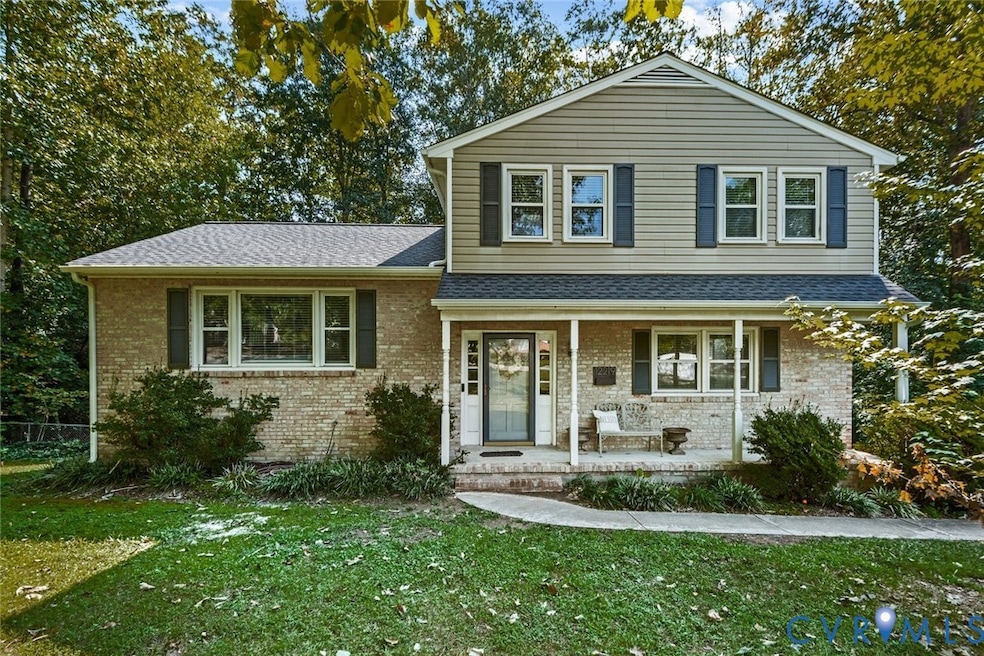 View of front facade featuring covered porch, brick siding, roof with shingles, and a front yard