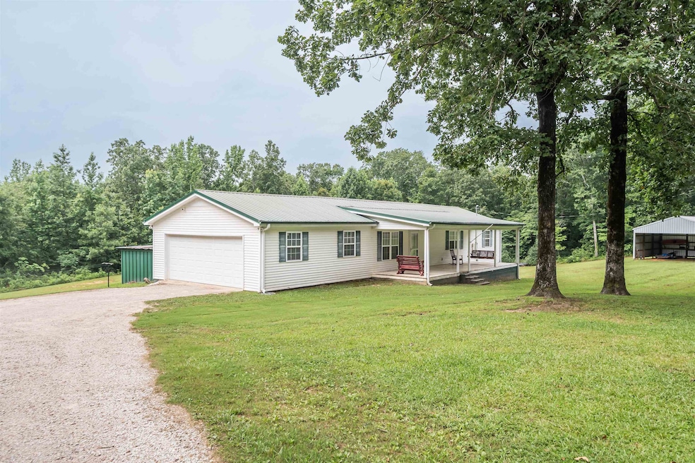 View of front facade featuring dirt driveway, a front yard, a metal roof, covered porch, and view of wooded area