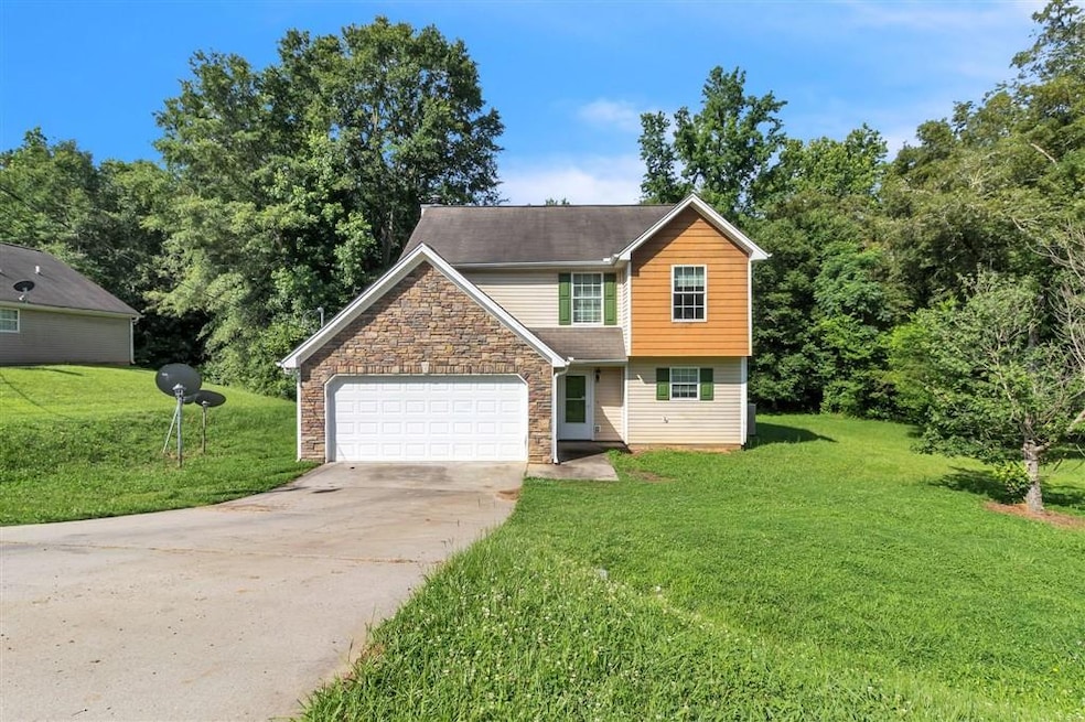 View of front of home featuring stone siding, driveway, a front lawn, and a garage