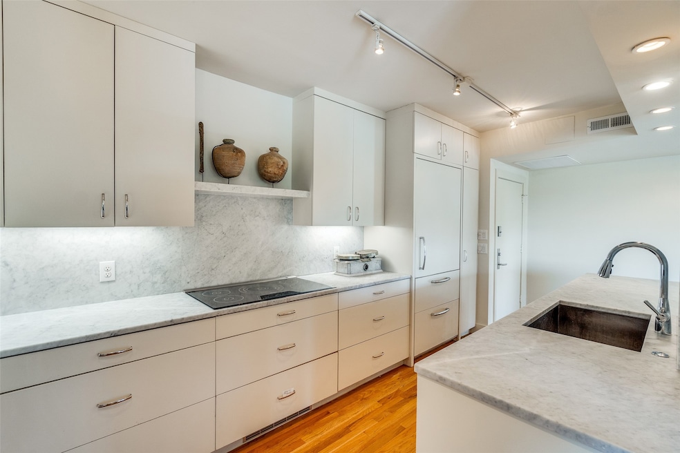 Kitchen with rail lighting, light wood-style flooring, decorative backsplash, light stone countertops, and black electric stovetop