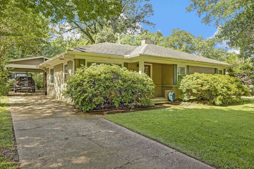 Ranch-style house featuring concrete driveway, a front yard, a chimney, a carport, and a shingled roof