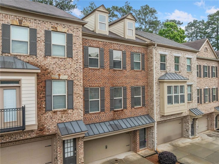 View of property with brick siding, an attached garage, driveway, and a standing seam roof
