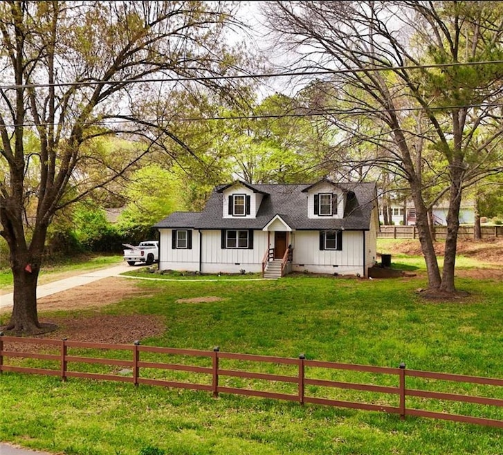 View of front of home with a fenced front yard, dirt driveway, roof with shingles, board and batten siding, and crawl spacer