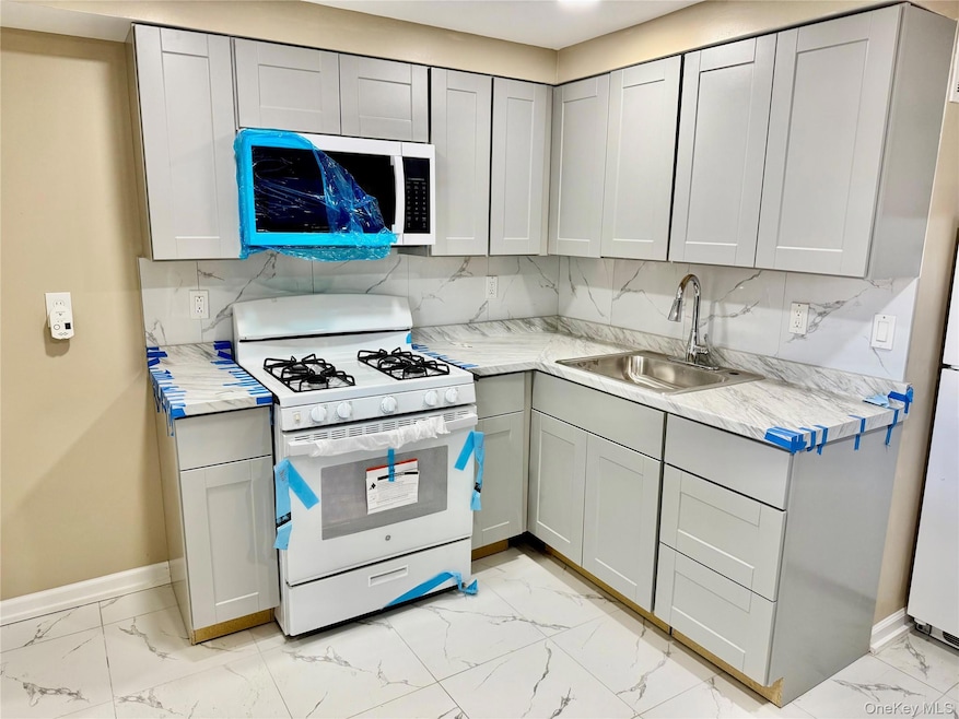 Kitchen with white appliances, backsplash, and light countertops