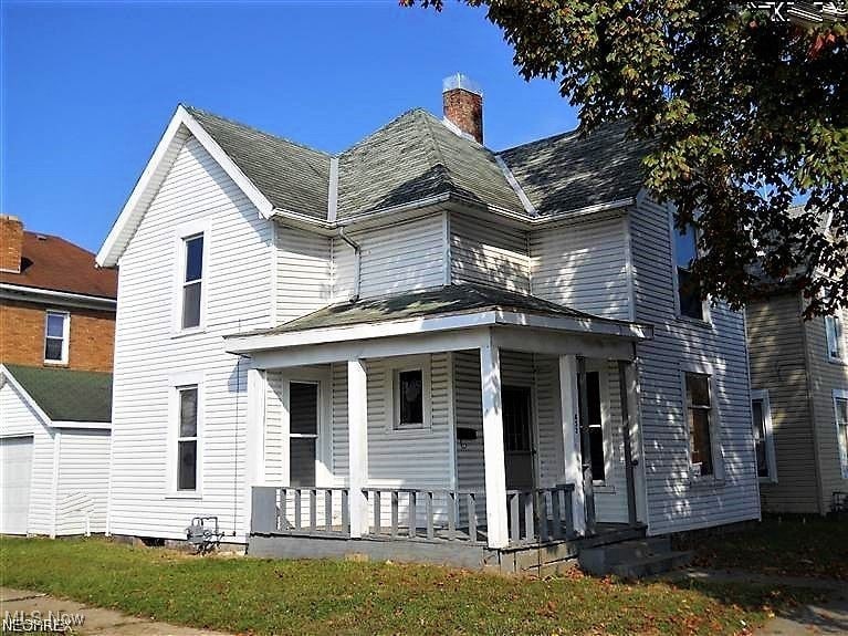 View of front of property featuring a porch, a chimney, and a garage