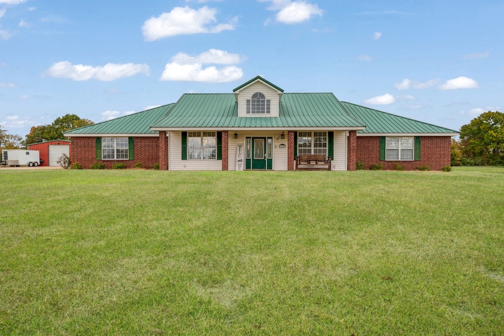 View of front facade featuring covered porch, a front lawn, a metal roof, and a garage
