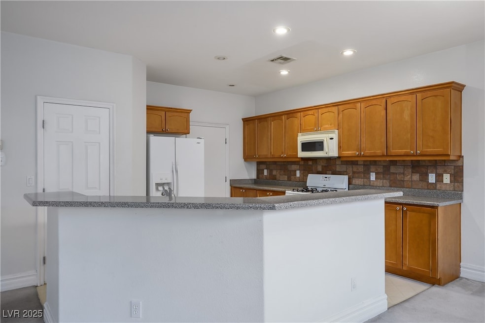 Kitchen with white appliances, decorative backsplash, brown cabinets, recessed lighting, and dark stone counters