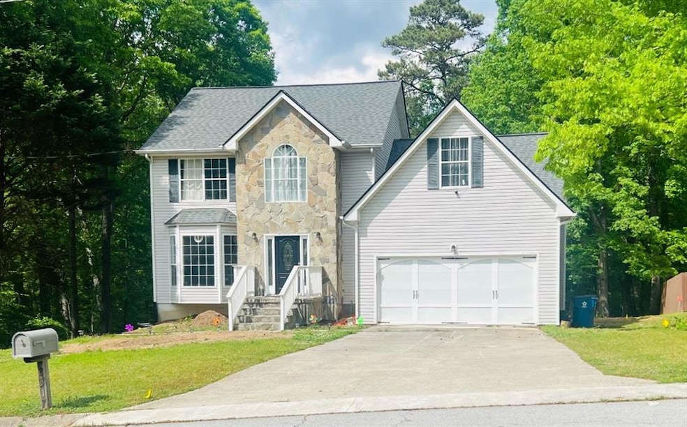 Colonial house with driveway, stone siding, a shingled roof, a front yard, and a garage
