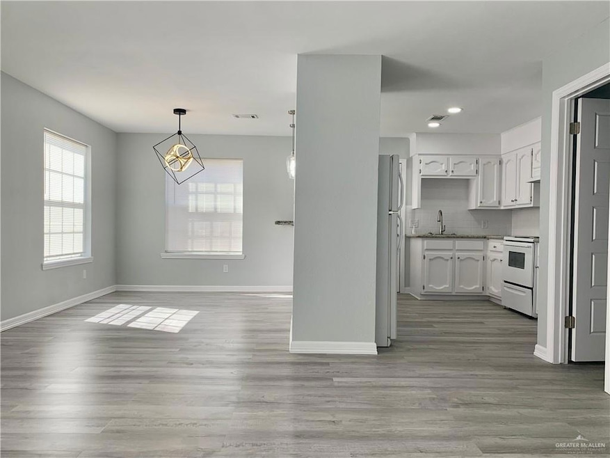 Kitchen featuring white cabinets, backsplash, white appliances, light wood-style floors, and hanging light fixtures
