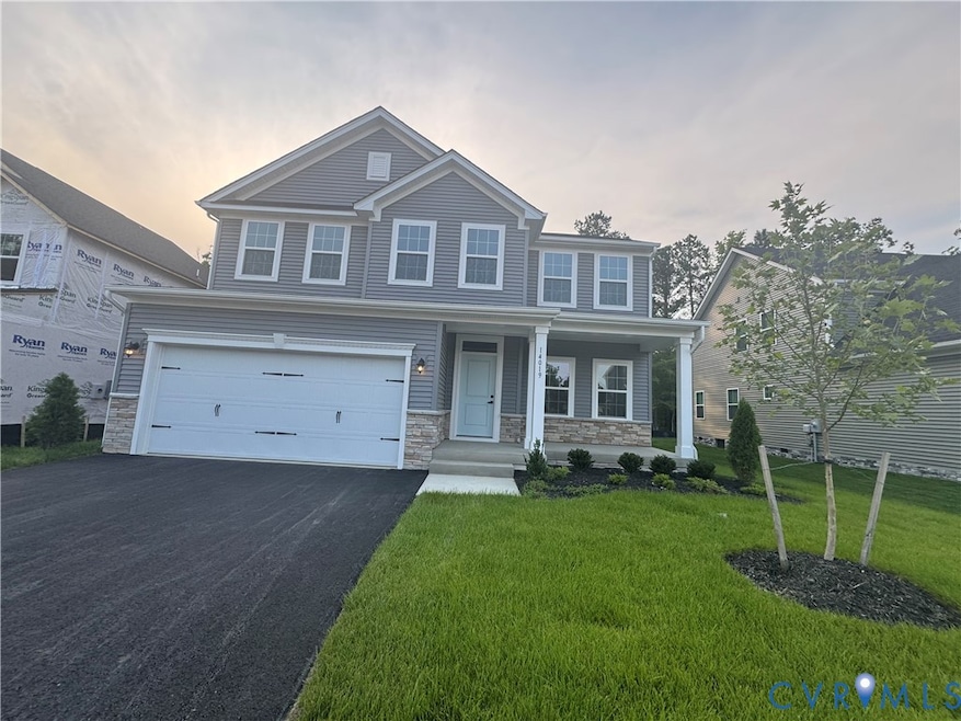 View of front of house with stone siding, driveway, covered porch, a front lawn, and a garage