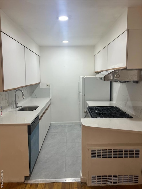 Kitchen featuring white cabinets, backsplash, radiator, light stone counters, and dishwashing machine
