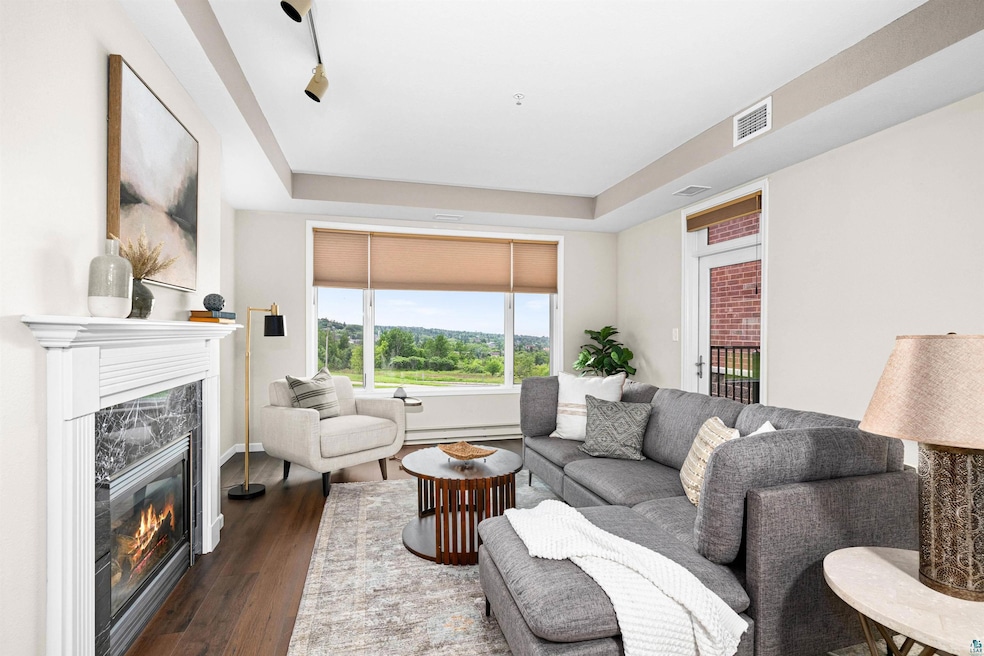 Living area featuring a raised ceiling, a high end fireplace, dark wood-style floors, and a baseboard heating unit