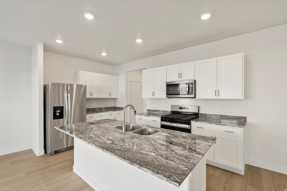 Kitchen with stainless steel appliances, dark stone counters, white cabinets, light wood-style flooring, and an island with sink