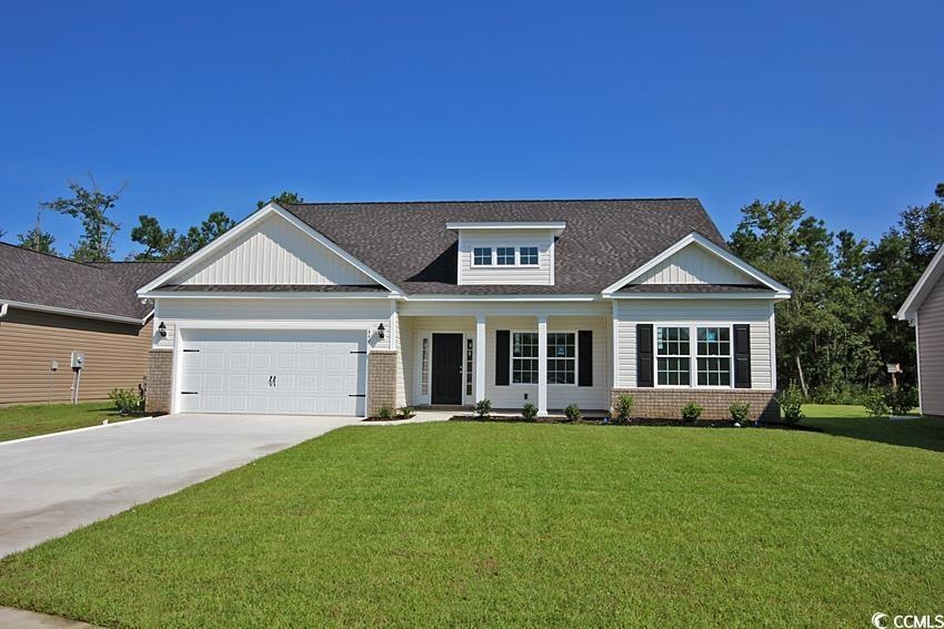 View of front facade featuring brick siding, a front yard, driveway, covered porch, and an attached garage