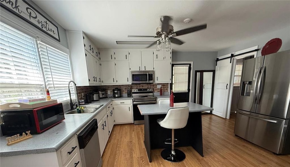 Kitchen with a barn door, appliances with stainless steel finishes, white cabinets, and light wood-type flooring