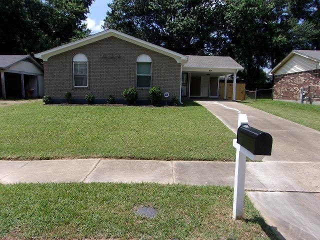 Single story home featuring concrete driveway, brick siding, an attached carport, and a porch