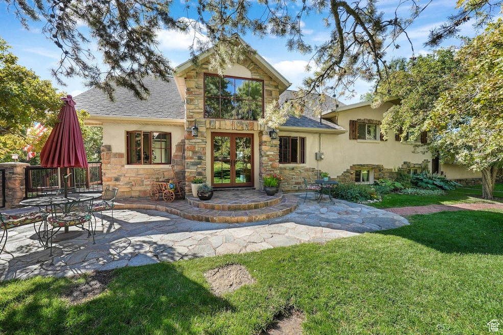 Rear view of house featuring stone siding, a patio, a shingled roof, and french doors