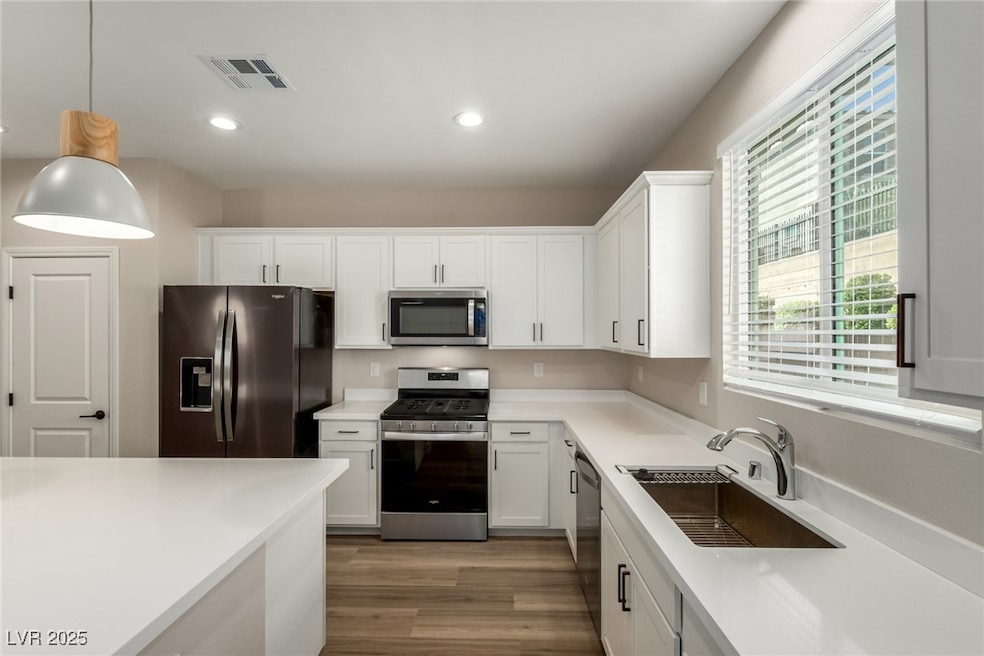 Kitchen featuring appliances with stainless steel finishes, white cabinets, pendant lighting, recessed lighting, and light wood-style flooring