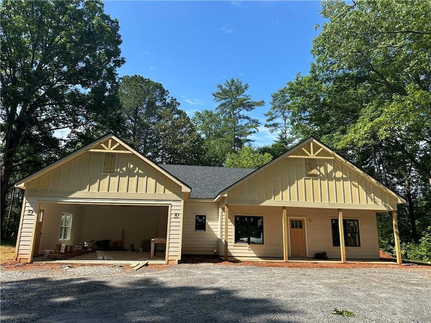 View of front of home featuring board and batten siding, a garage, covered porch, a shingled roof, and gravel driveway