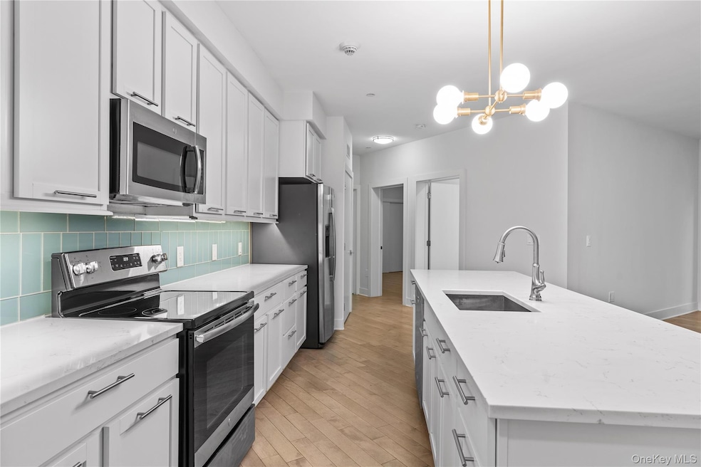 Kitchen with stainless steel appliances, an island with sink, light wood-style flooring, and white cabinets