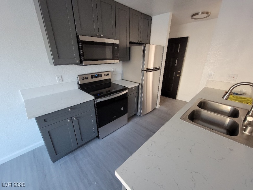 Kitchen featuring appliances with stainless steel finishes, a sink, light wood finished floors, and light stone counters